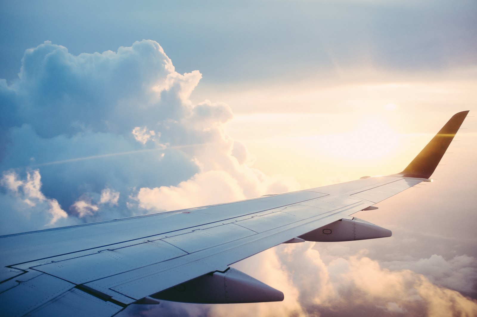 Aircraft wing above the clouds at sunrise, representing overseas travel for work