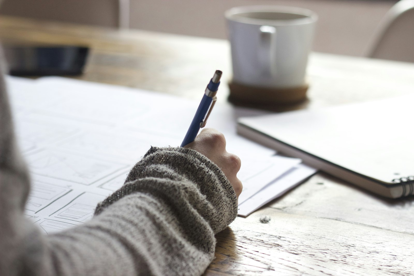 Person writing notes on paper at a desk with a coffee
